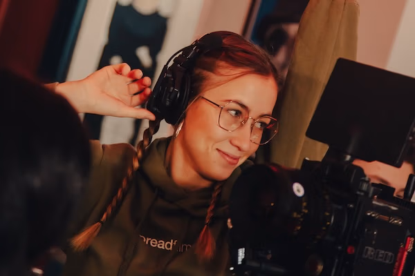 Clara Mitglied von Spreadfilms mit Kopfhörern und Brille lächelt, während sie an einer Kamera arbeitet