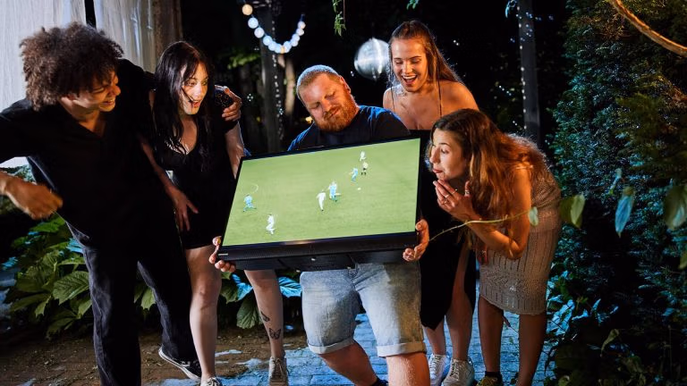 Gruppe feiert gemeinsam mit einem tragbaren TV – Fußballspiel im Freien, aufgenommen für eine Spreadfilms-Produktion für Imtron PEAQ