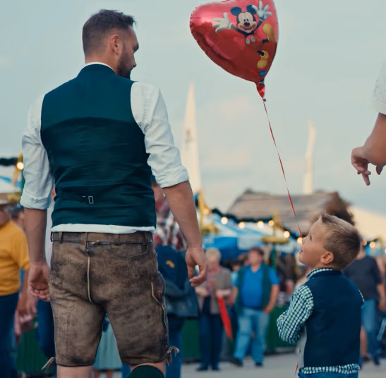 Foto von einem Mann in Trachtenkleidung auf einem Fest neben einem Jungen der einen roten Herzballon hält - aus einem Eventfilm von Spreadfims