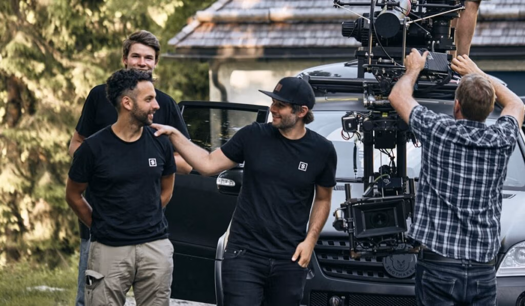 Behind-the-Scenes Szene von Spreadfilms: Mitarbeiter lachen gemeinsam vor einem grauen Auto und Kamera Setup