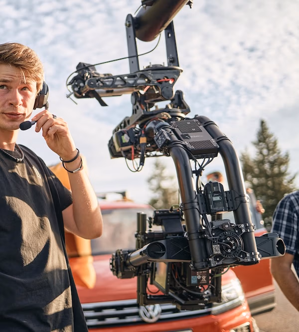 Filmcrew-Mitglied von Spreadfilms mit Headset neben großer Kamerakran-Rig vor einem roten VW