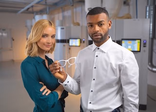 Mann zeigt einer Frau ein weißes 3D-gedrucktes Brillengestell, sie befinden sich in einem technischen Labor - ein Foto von Spreadfilms