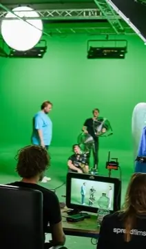 Filmcrew bei Dreharbeiten im Greenscreen-Studio mit Kamera, Licht und Monitor für Live-Vorschau.