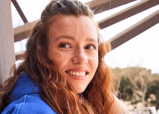 Junge Frau mit langen lockigen Haaren lächelt in einer sonnigen Außenszene von Spreadfilms