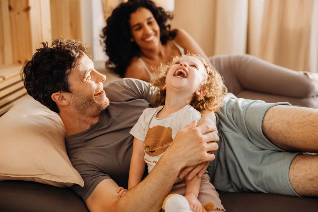 Lachendes Kind, das mit zwei Erwachsenen auf einem Sofa spielt - Bild aus dem Wenatex Werbevideo von Spreadfilms